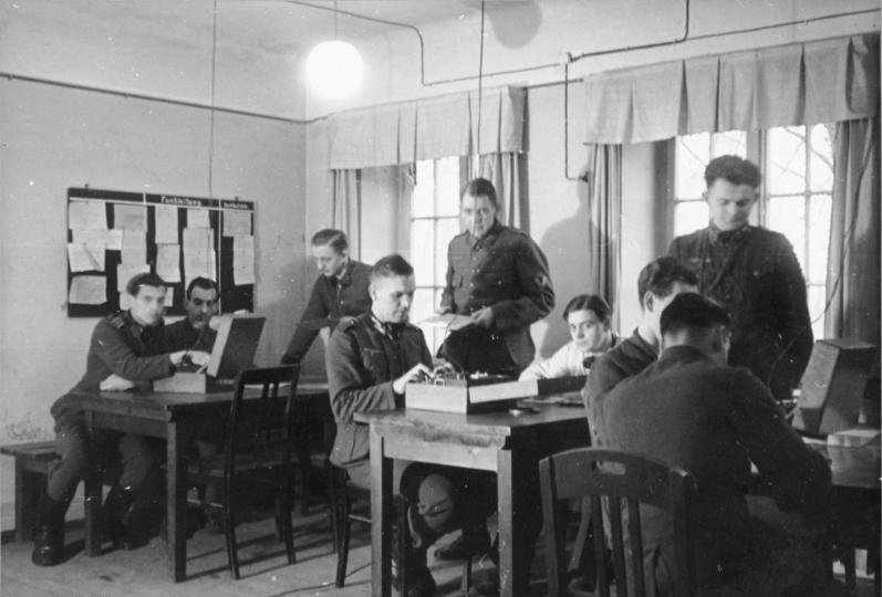 Figure 4 — German signals personnel operating an Enigma in the field. Ciphering was typically a two- or three-person job: one keyed the text, one read the lamps, one worked the Morse key. File:Bund…
